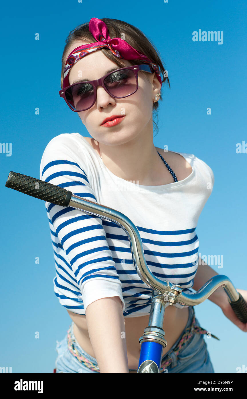 La bellissima ragazza con la bicicletta sulla passeggiata a mare contro il cielo blu Foto Stock