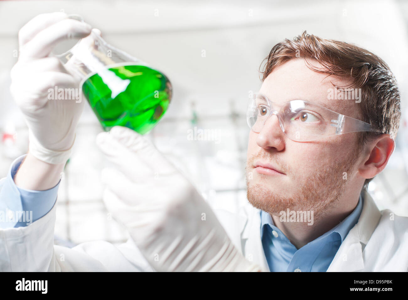 Germania, giovane scienziato controllo liquido verde in beute di Erlenmeyer Foto Stock