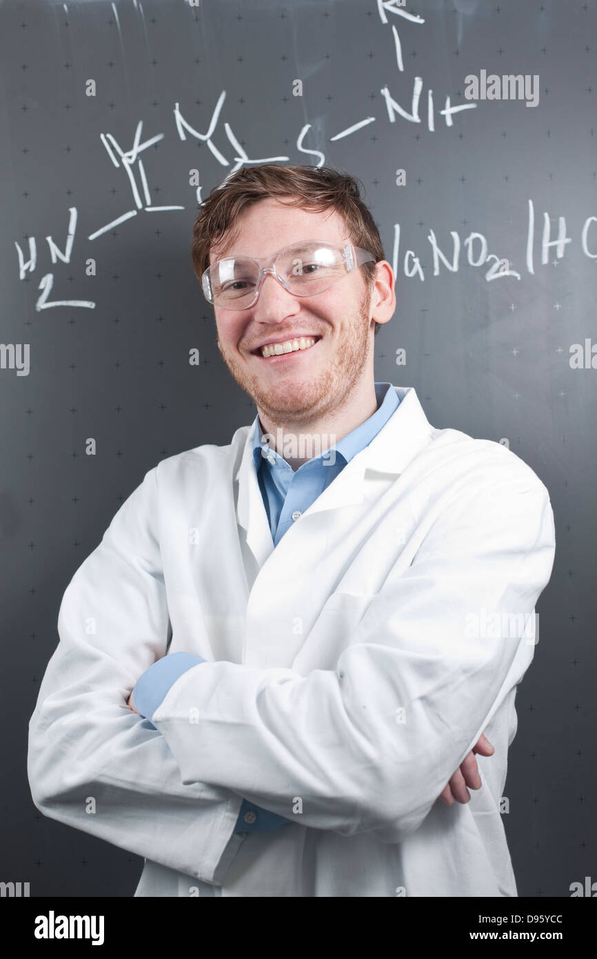 Germania, Ritratto di giovane scienziato in piedi di fronte a equazione chimica su chalk board, sorridente Foto Stock