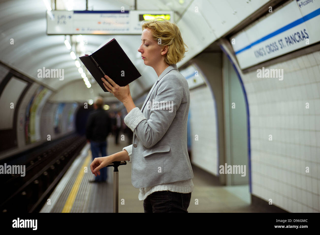 Una donna che legge un libro mentre è in attesa per un metro di Londra treno tubo sulla piattaforma di Kings Cross St Pancras. Foto Stock
