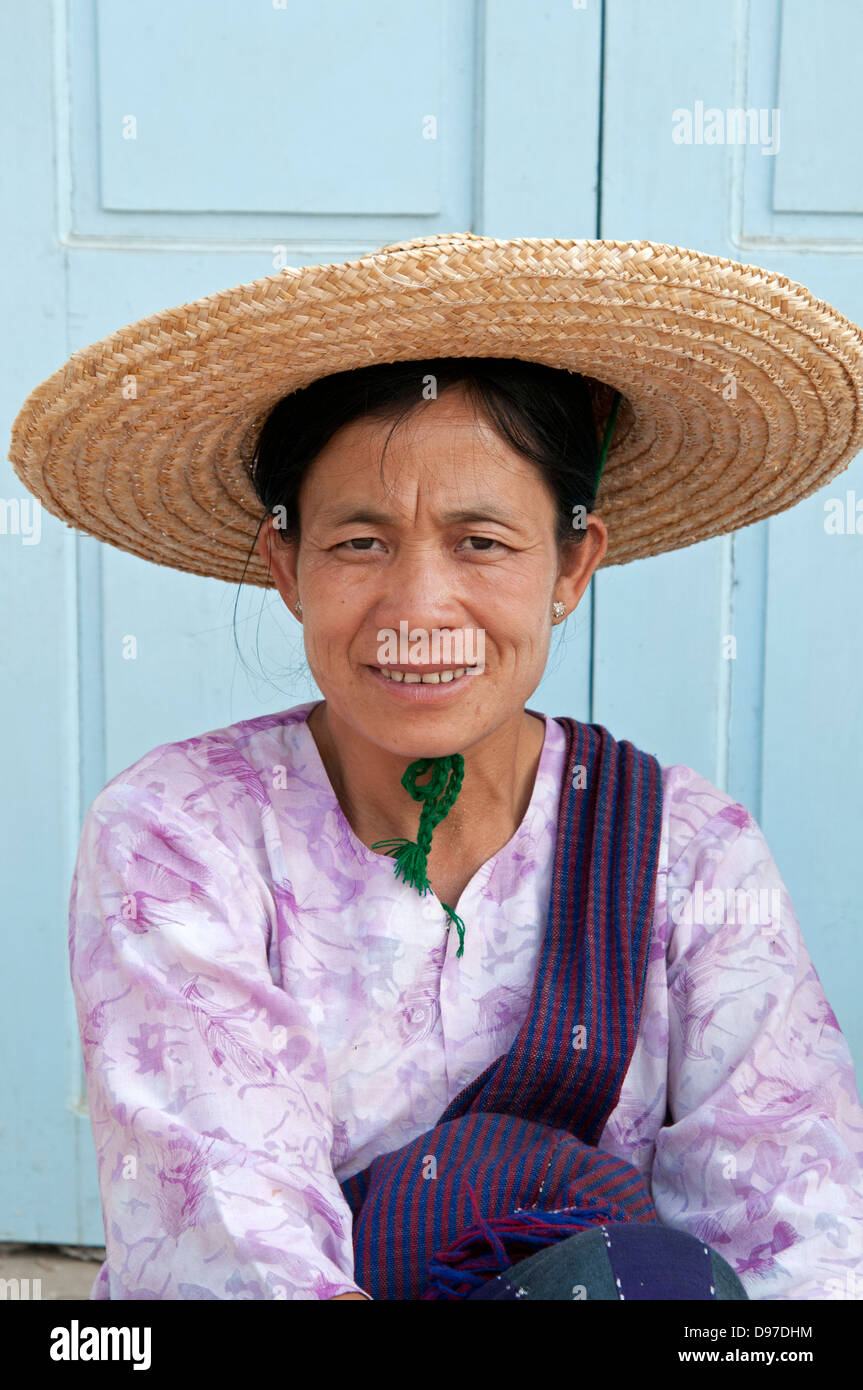 Donna che indossa cappello di paglia seduta da blue porta in legno MYANMAR Birmania Foto Stock