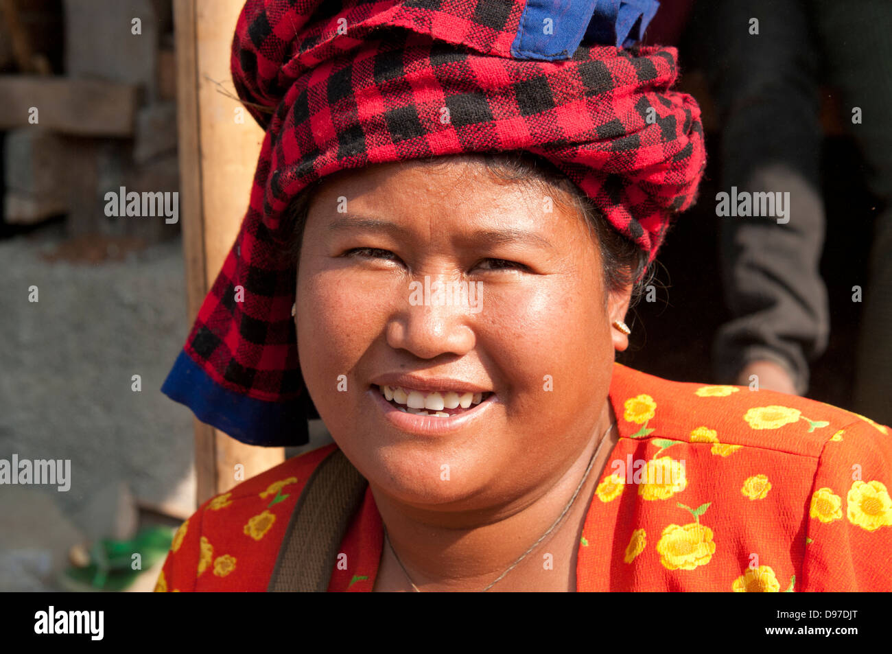 Donna che indossa rosso luminoso controllato copricapo sorridente in telecamera in un mercato in Myanmar (Birmania) Foto Stock