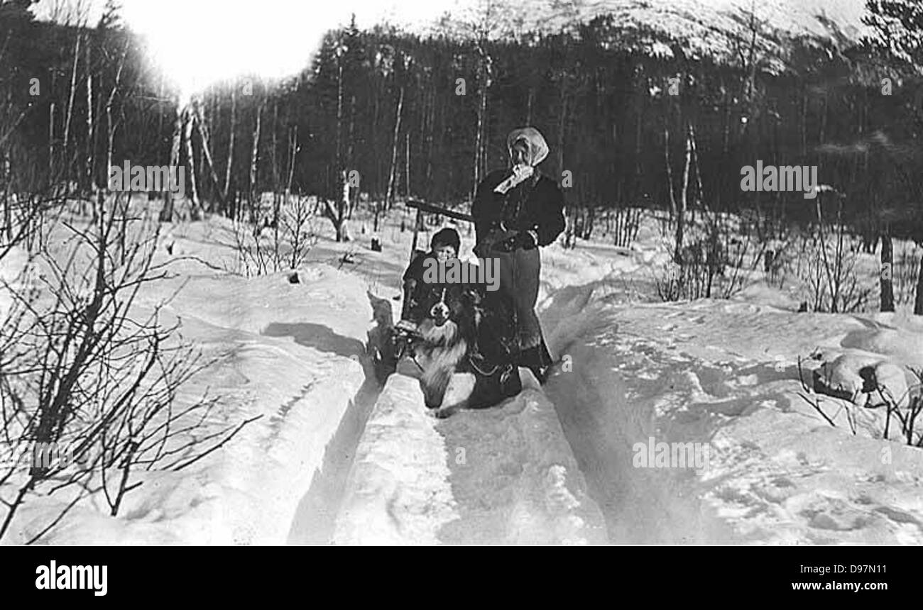 Questa immagine mostra una donna con un bambino, un cane e una slitta nella neve, probabilmente in Alaska, catturando un momento di attività invernale in un ambiente freddo e innevato. Foto Stock