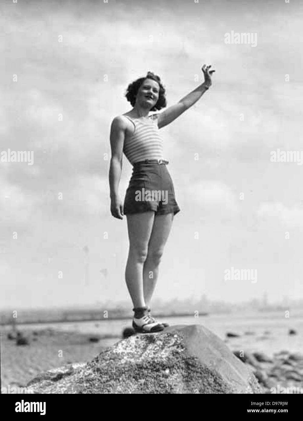 Donna in costume da bagno sventolare mentre in piedi su una grande roccia su una spiaggia, probabilmente stato di Washington Foto Stock