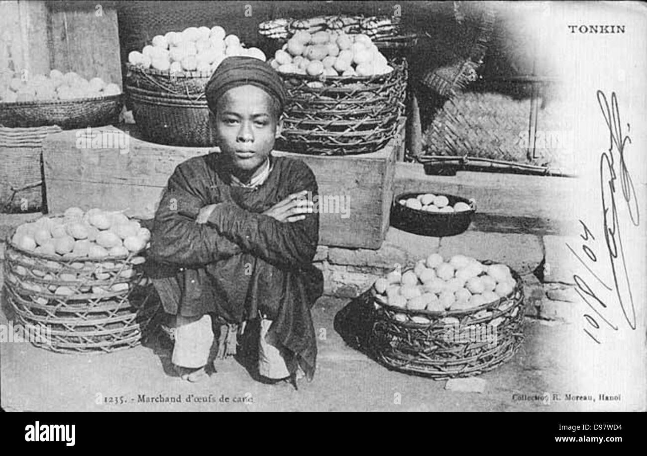 Un commerciante vietnamita di uova che vende uova in un mercato, raffigurato in un ambiente tradizionale con cesti e cappelli. Il mercante è vestito con una tunica e la foto cattura la vita quotidiana in Vietnam. Foto Stock