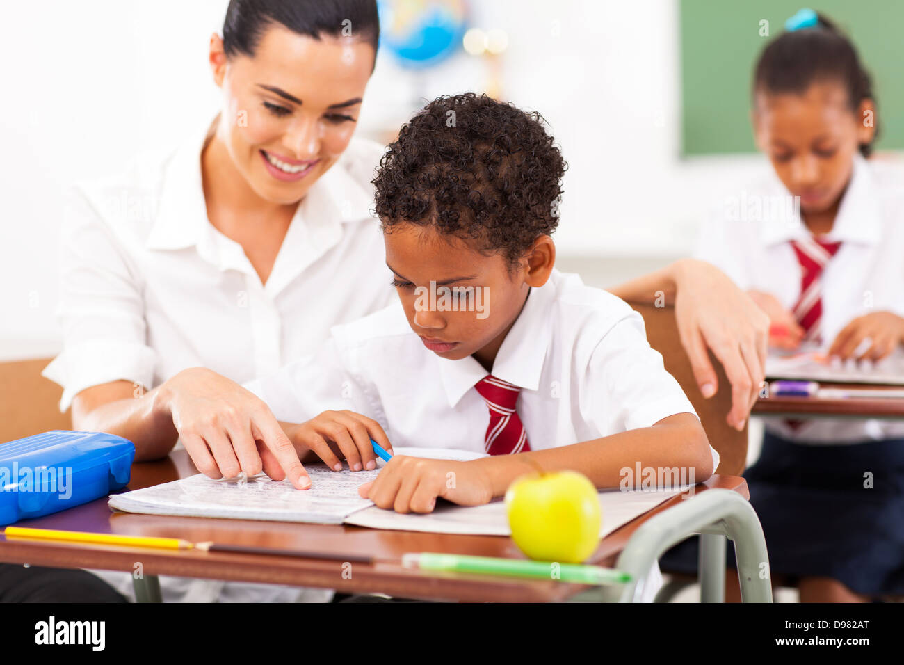 Caring insegnante di scuola elementare aiutare lo studente in aula Foto Stock