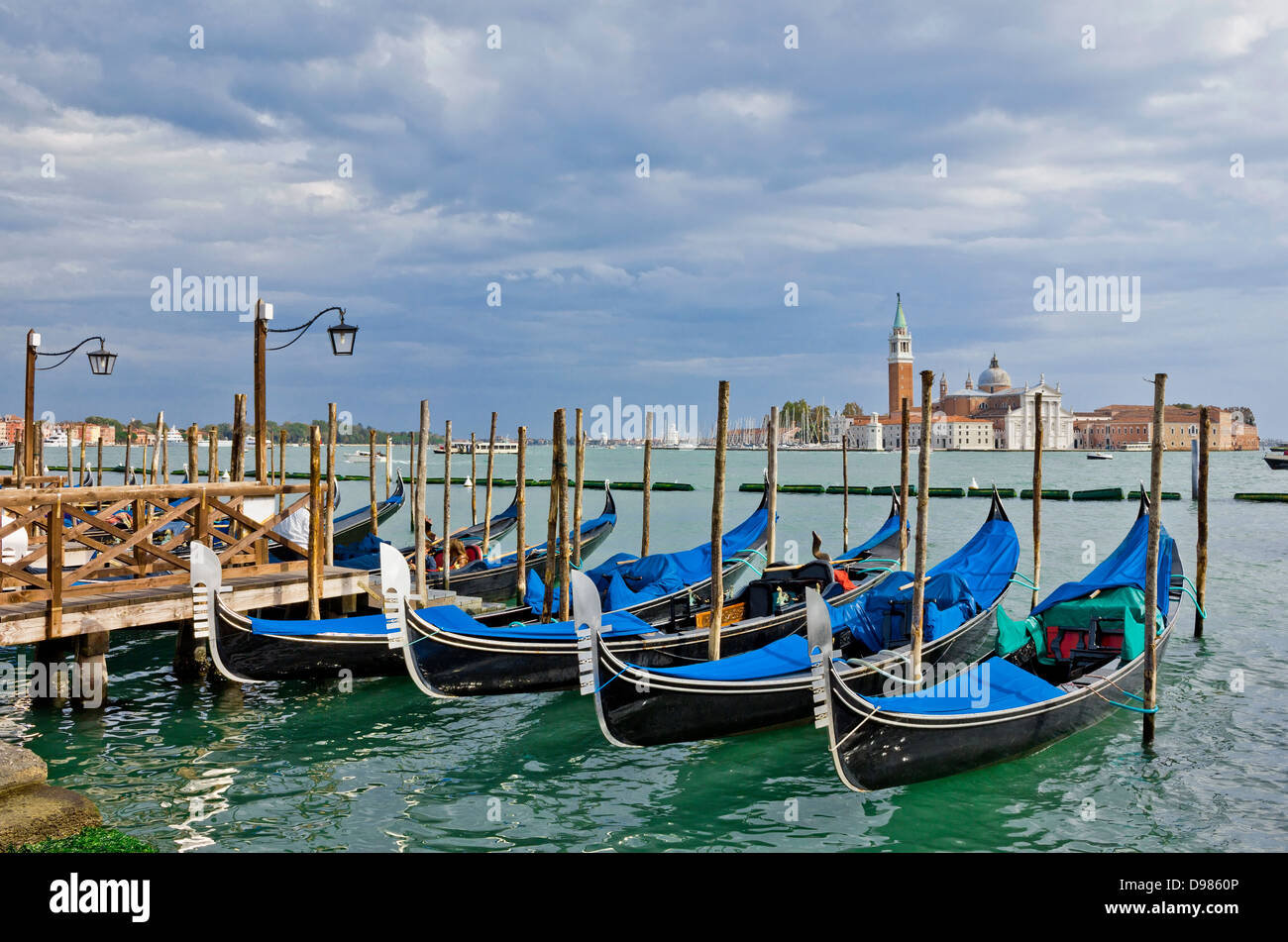 Gondole in attesa per i turisti nei pressi di Piazza San Marco a Venezia. Vista con drammatico cielo verso San Giorgio Maggiore. Foto Stock