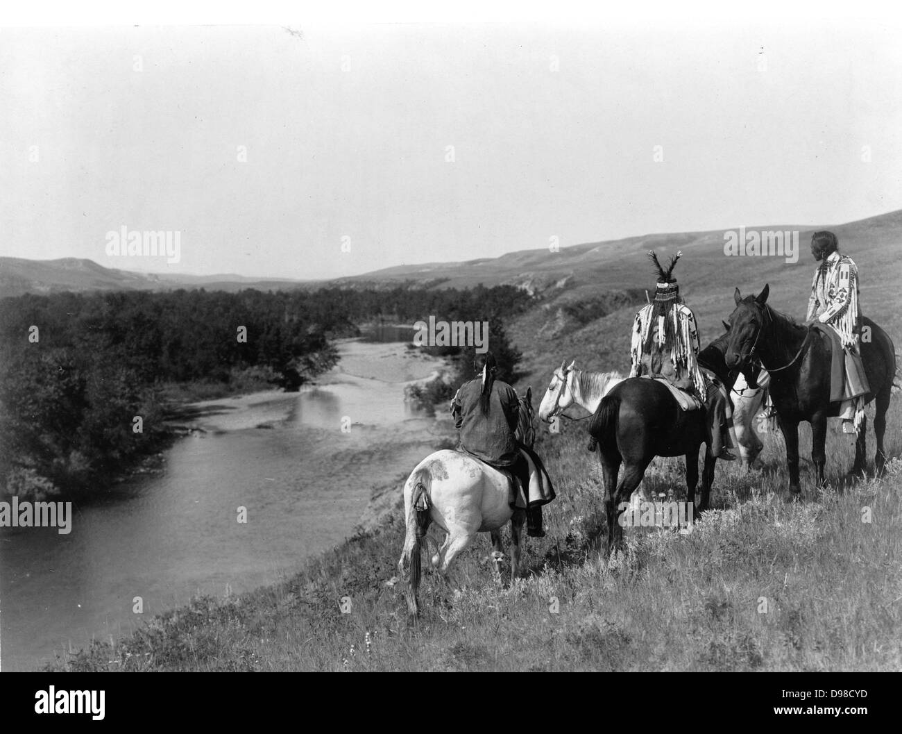 Tre Piegan indiani e quattro cavalli sulla collina sopra il fiume, 1910. Fotografia di Edward Curtis (1868-1952). Foto Stock