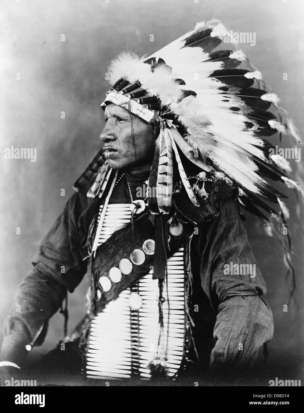 Uccello Rosso, Indiani Sioux, mezza lunghezza ritratto, seduto, rivolto verso sinistra, INDOSSARE COPRICAPO piumato, c1908. Fotografia di John A. JOHNSON Foto Stock