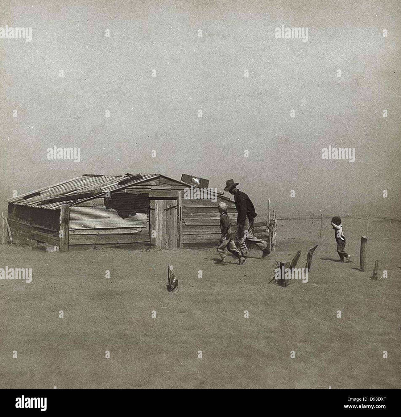 Tempesta di polvere, Coppa America, 1930s. L'uomo e per i ragazzi a camminare verso la capanna in legno che viene gradualmente coperto da wind-polvere soffiata. Piccolo ragazzo sta tenendo la sua mano per proteggere il suo volto. Foto Stock