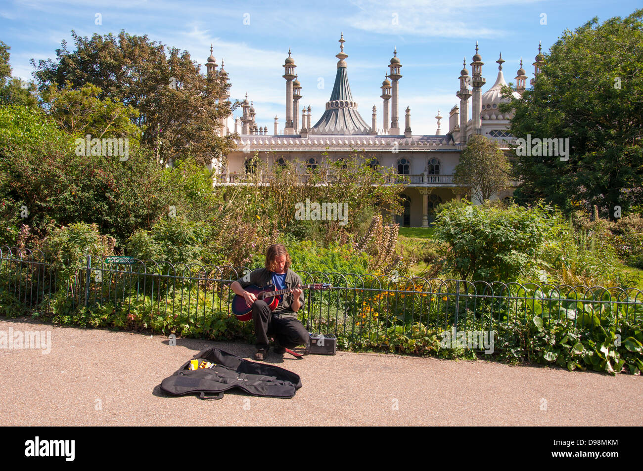 Un senzatetto, musicista di strada da suonare la chitarra attraverso un amplificatore portatile, in un parco vicino al Padiglione di Brighton, Inghilterra, Regno Unito. Foto Stock