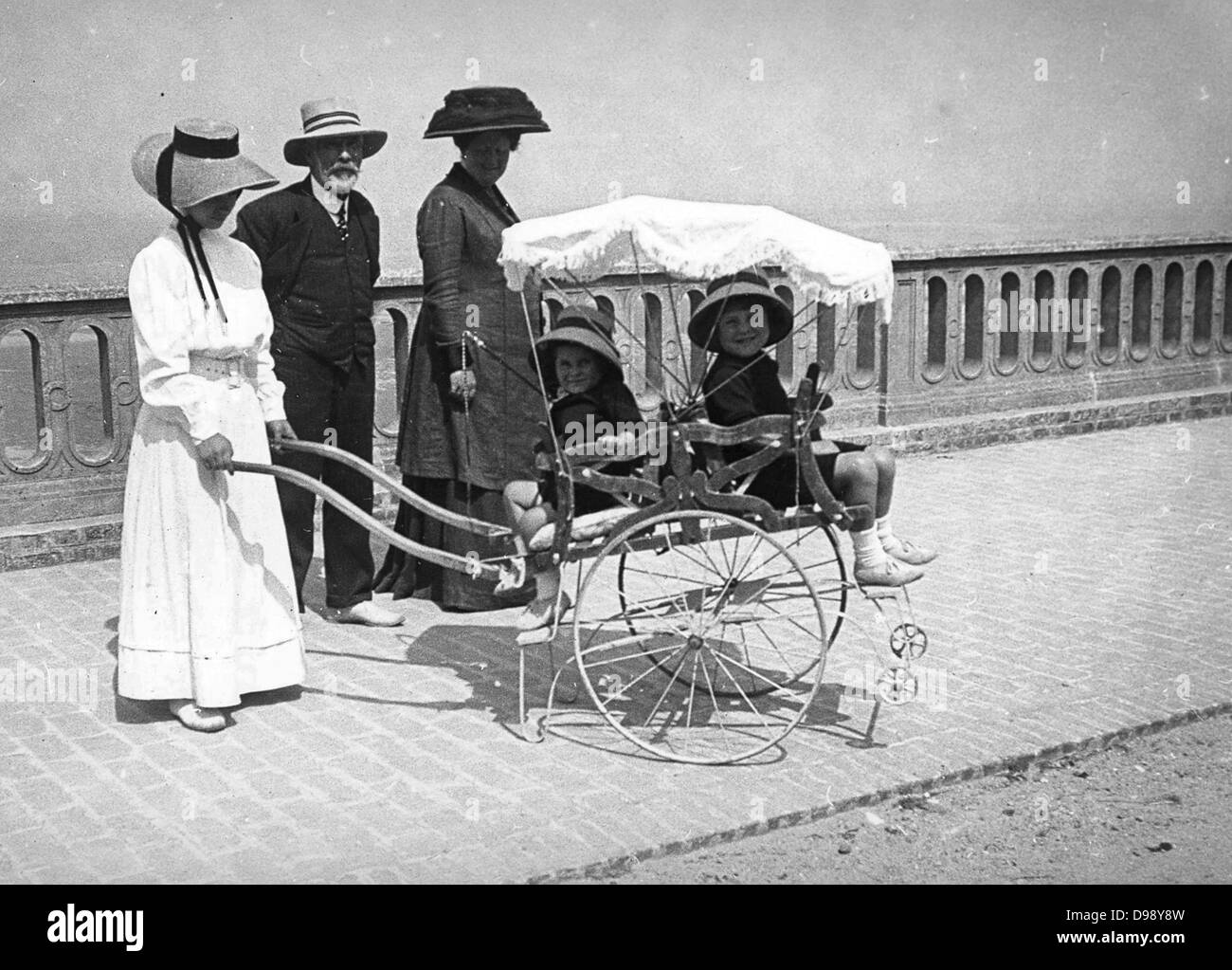 Donna francese (possibilmente una bambinaia), spingendo una carrozzina con due bambini. Circa 1900 Foto Stock