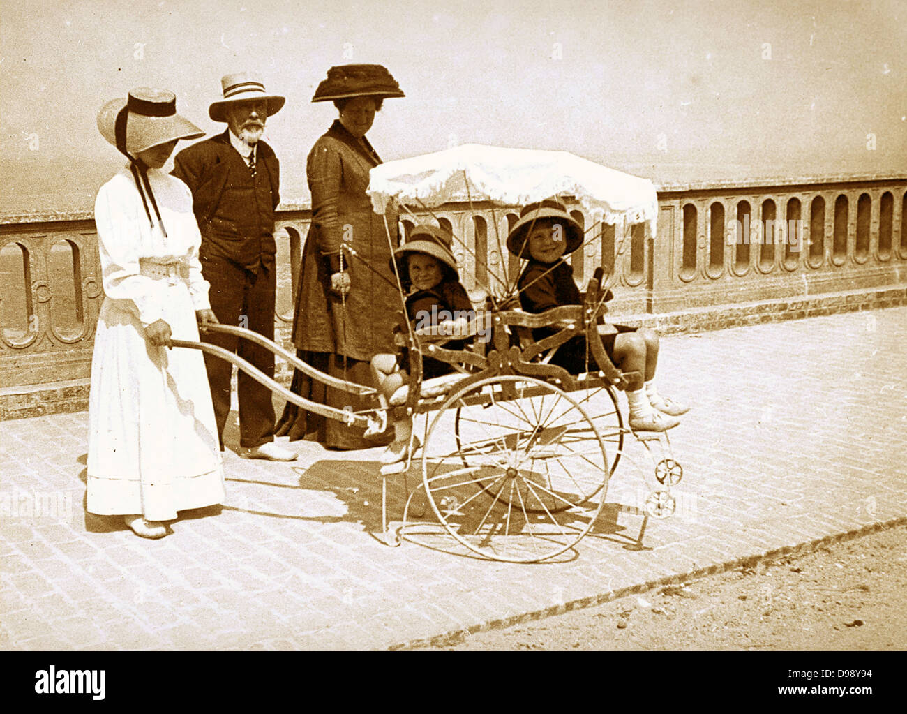 Donna francese (possibilmente una bambinaia), spingendo una carrozzina con due bambini. Circa 1900 Foto Stock