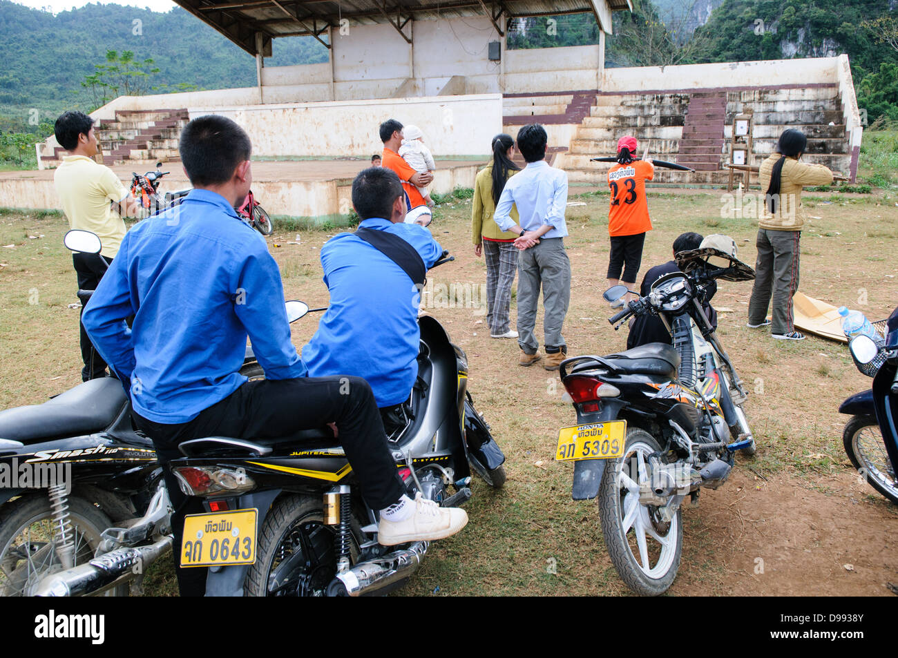 VIENG XAI, Laos - gli spettatori studenteschi si allineano sui loro scooter e moto per guardare una gara di balestra su un campo di gioco sterrato tra i terreni accidentati vicino a Vieng Xai nel nord-est del Laos. L'evento locale attira partecipanti e spettatori dai villaggi circostanti in questa regione rurale. Foto Stock