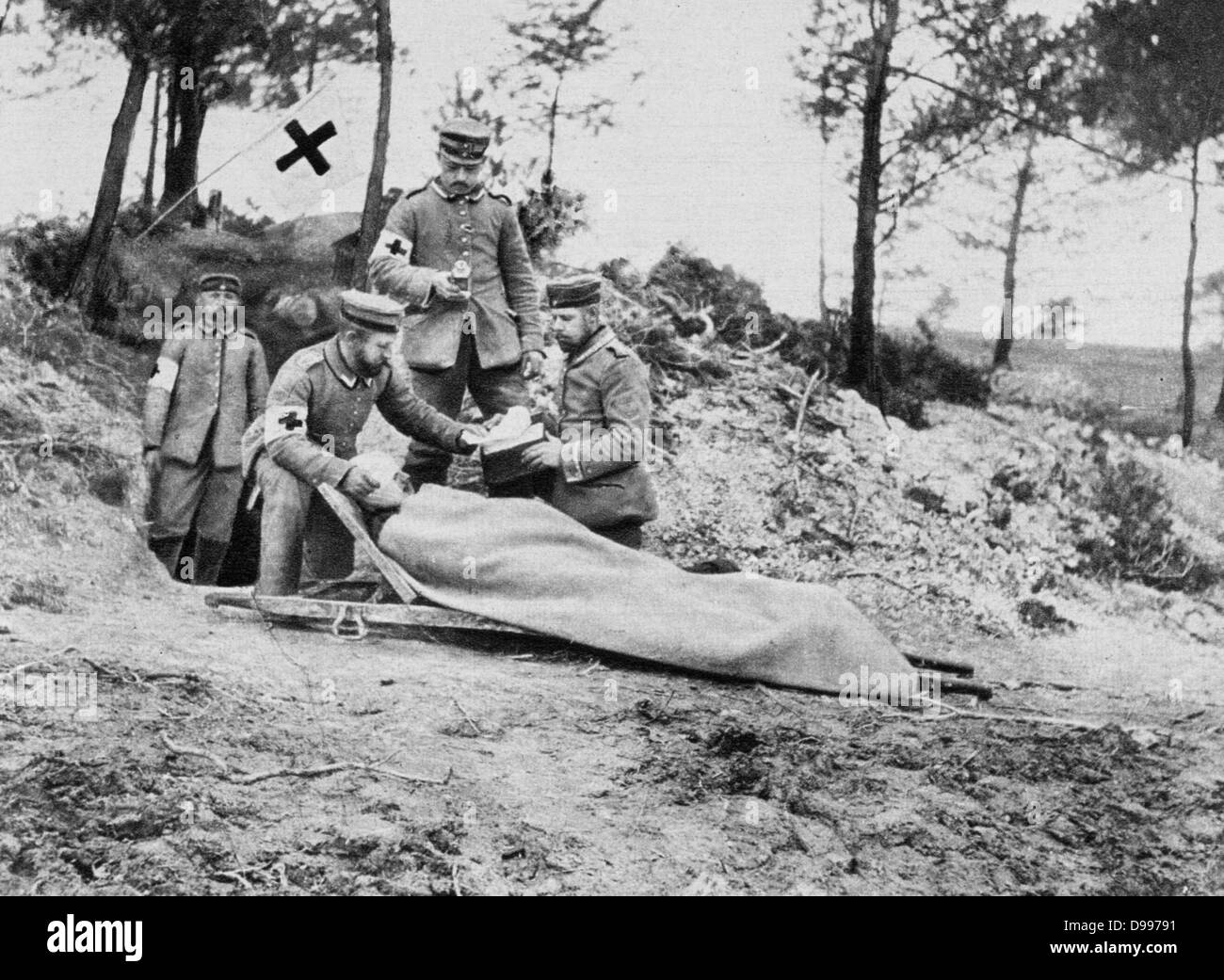 I Guerra Mondiale 1914-1918: ferito soldato tedesco su una barella che viene trattata dietro le trincee da un campo team medico visualizzando il simbolo della Croce Rossa, 1915. Medicina in primo luogo gli aiuti Warfare Casualty Foto Stock
