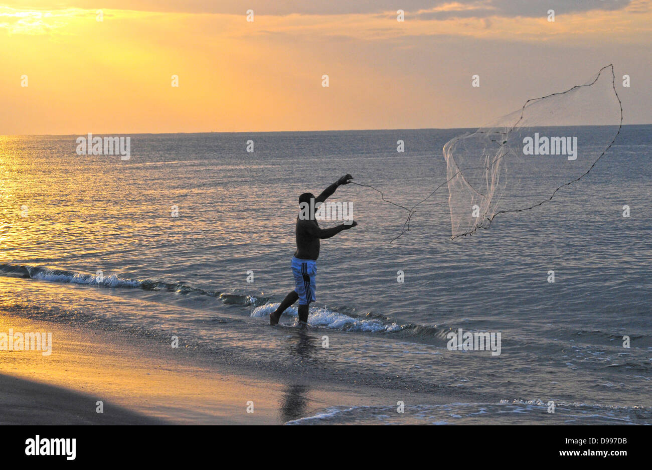 Giovane pescatore di gettare una rete da pesca nell'oceano Foto Stock