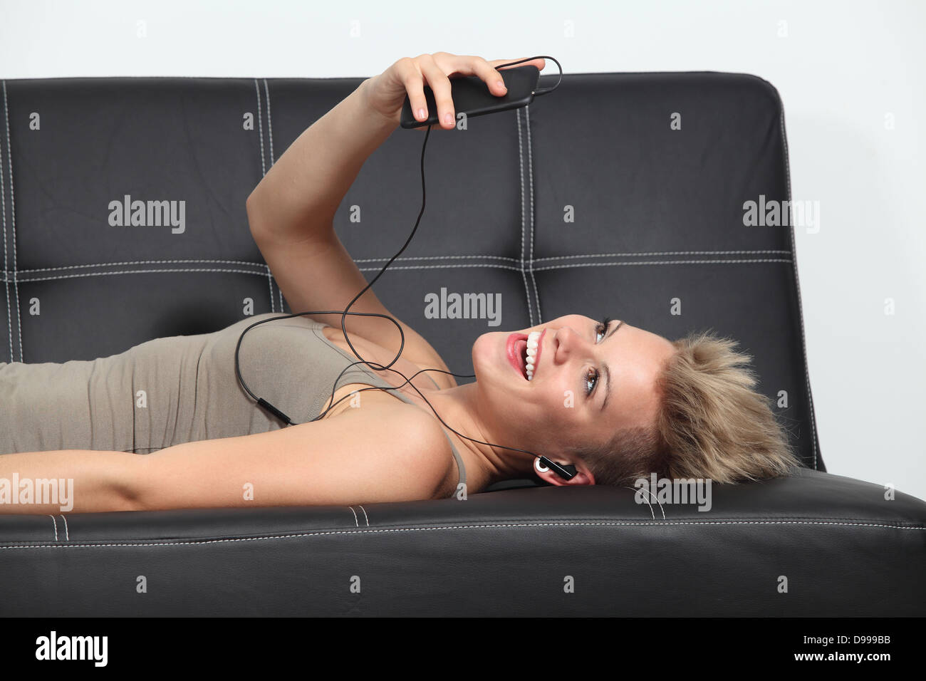 Profilo di una donna a casa sdraiato su un lettino ascoltando la musica da uno smartphone Foto Stock