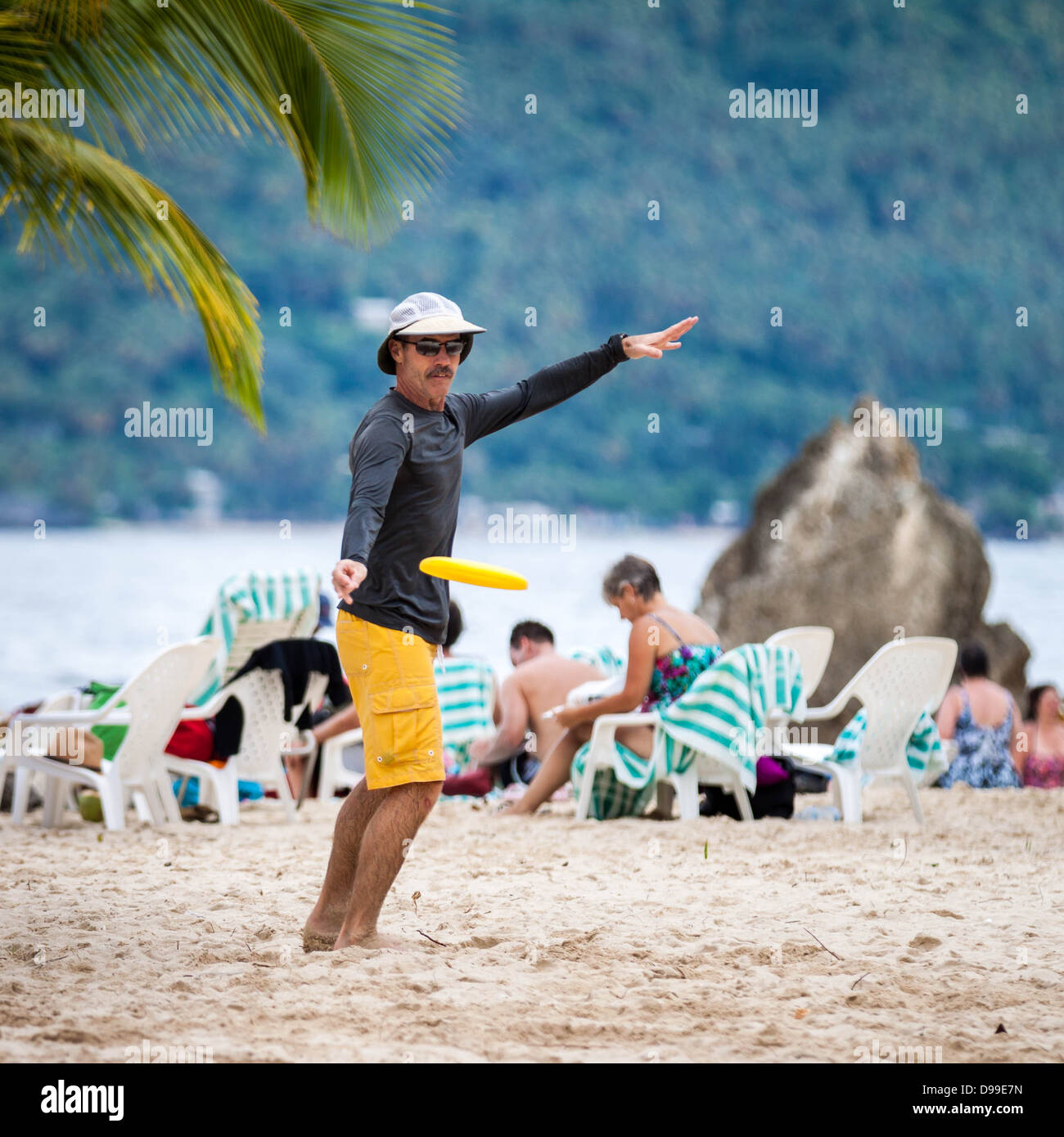 L'uomo trowing un frisbee giallo su una spiaggia tropicale Foto Stock