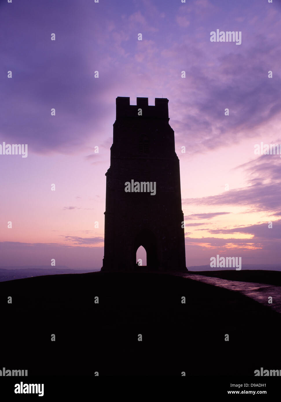 Le rovine di una torre di San Michele Cappella sulla cima di Glastonbury Tor, Somerset, visto come una silhouette contro un Cielo di tramonto. Figura incappucciati in archway. Foto Stock