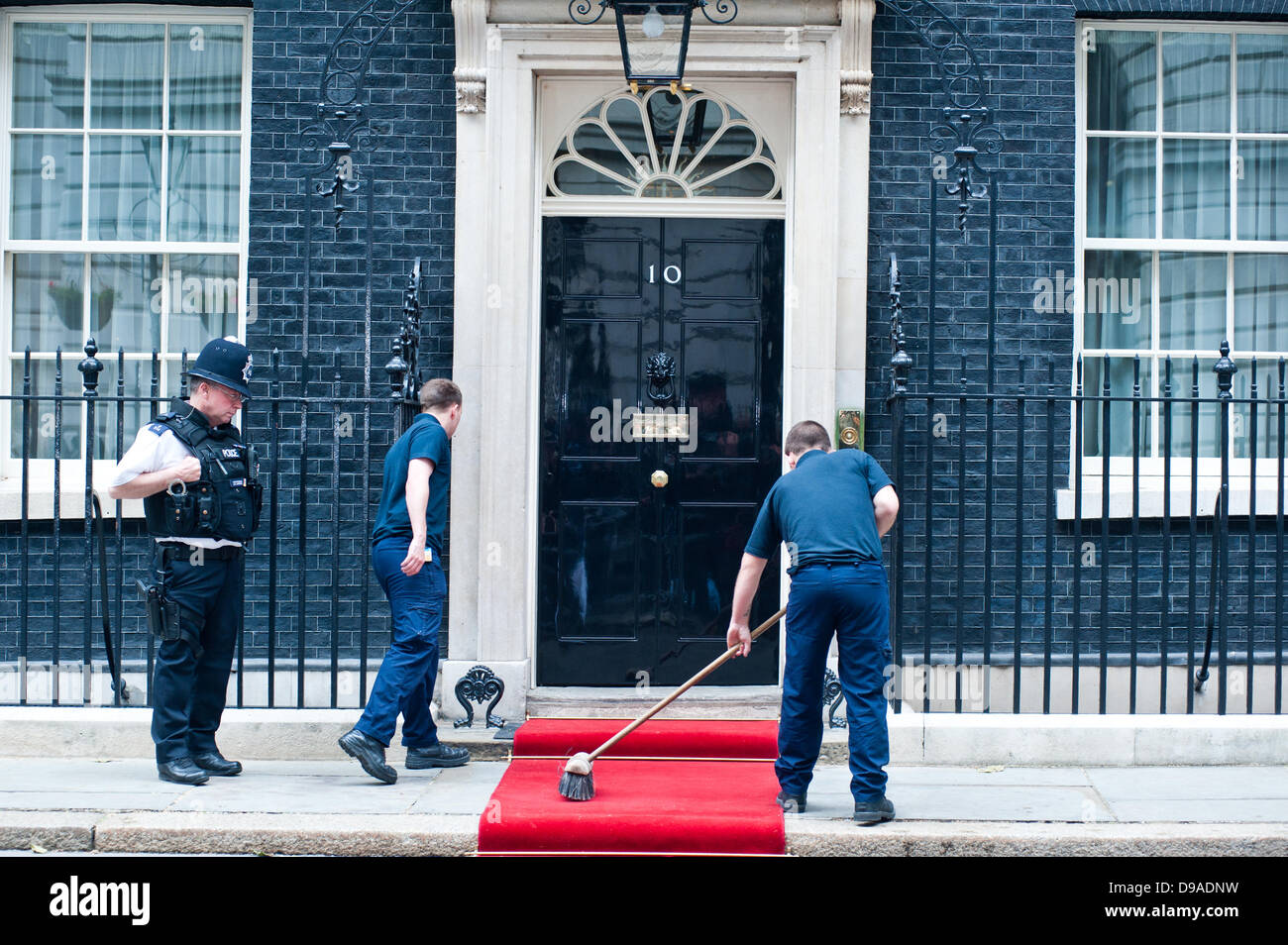 London, Regno Unito - 16 Giugno 2013: un uomo spazza il tappeto rosso davanti a 10 Downing Street prima dell'arrivo il presidente russo Vladimir Putin a causa di incontrare il Primo Ministro David Cameront o discutere la Siria in vista del G8. Credito: Piero Cruciatti/Alamy Live News Foto Stock