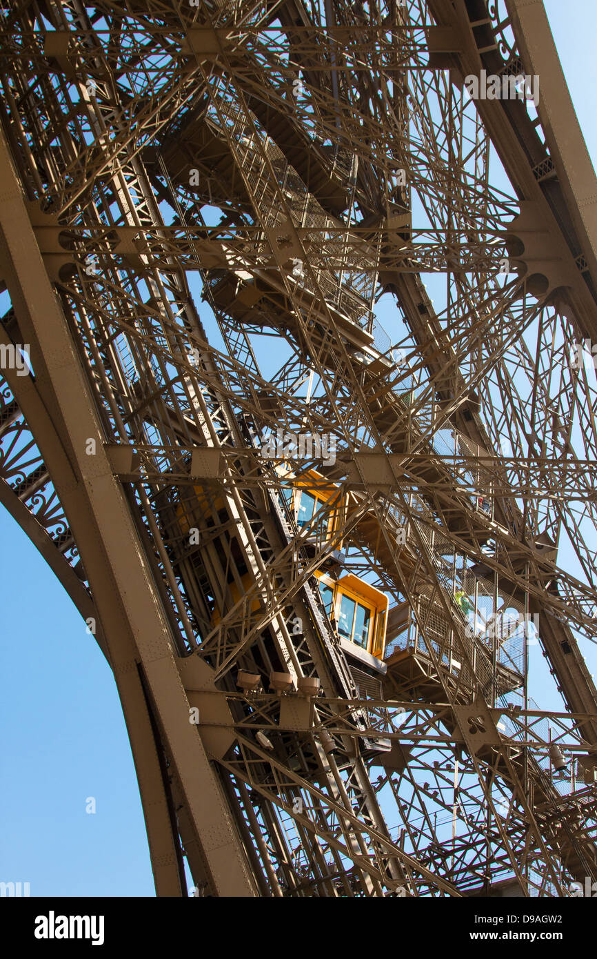 Due arancio brillante ascensori arrampicata Torre Eiffel trave come turisti a piedi giù passaggi adiacenti Foto Stock