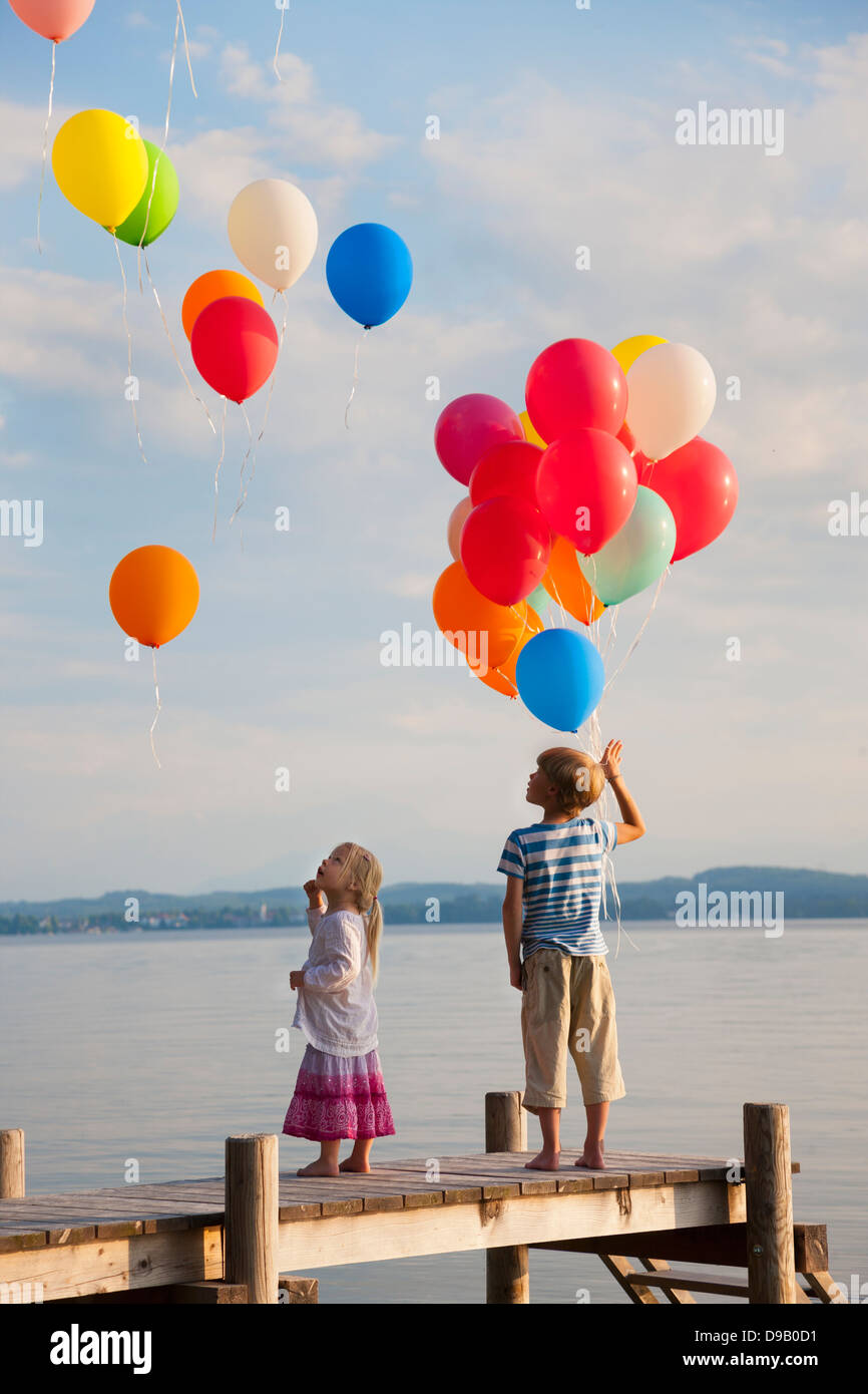 In Germania, in Baviera, un ragazzo e una ragazza in piedi sul molo, battenti palloncini a Lago di Starnberg Foto Stock