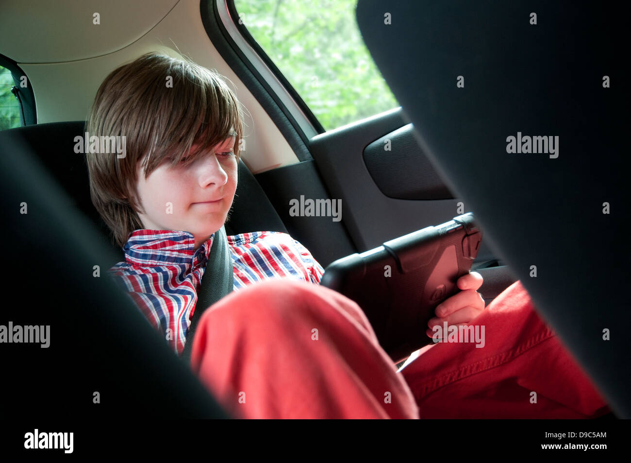 ragazzo giovane maschio che usa il mini tablet ipad nella sella posteriore dell'auto Foto Stock