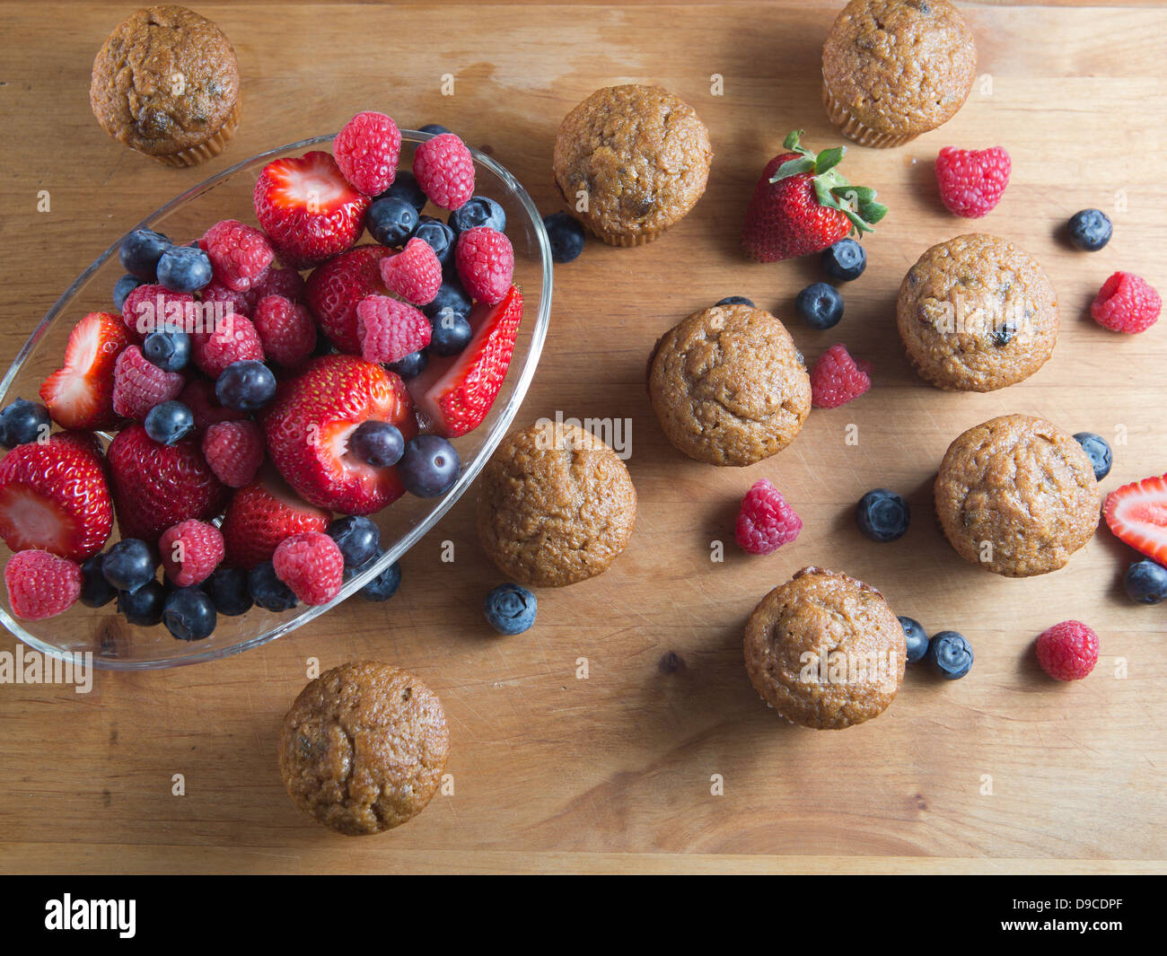 Frutta muffin appena sfornato collocato su un tavolo di legno a fianco di fragole, lamponi e mirtilli. Foto Stock