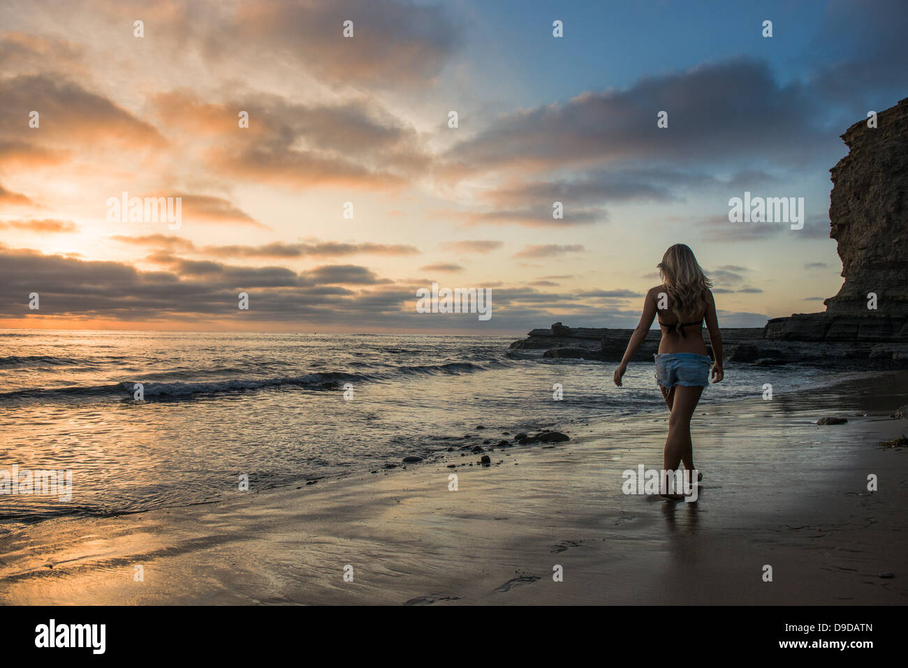 Giovane donna camminando sulla spiaggia al tramonto, vista posteriore Foto Stock