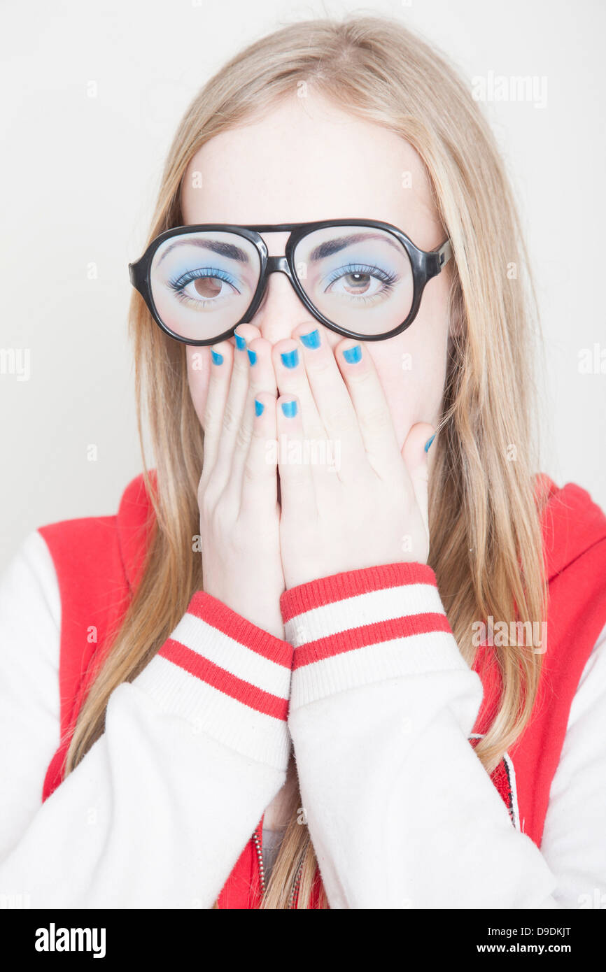 Ragazza indossando occhiali finti con le mani che coprono la bocca Foto Stock
