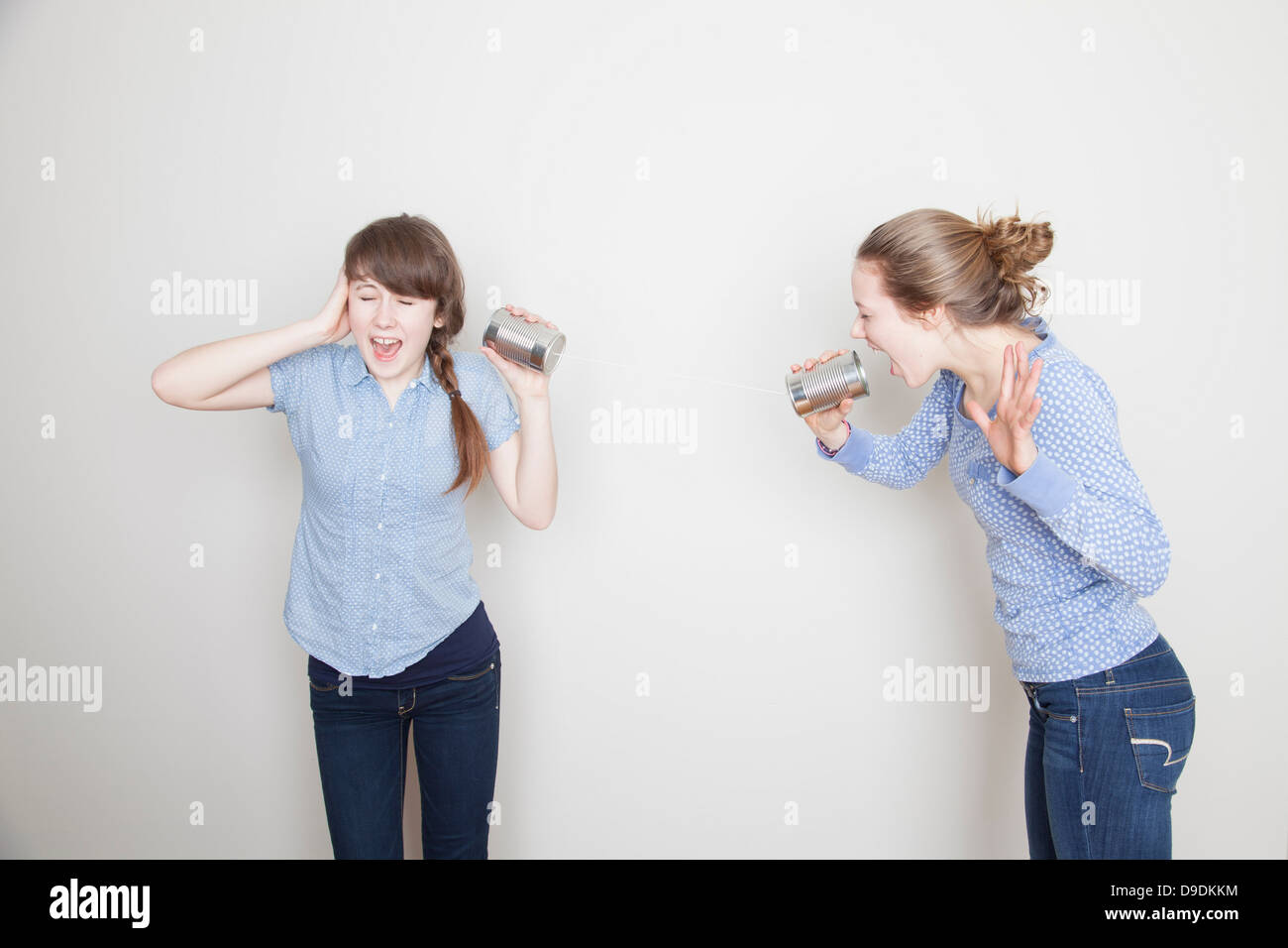 Due ragazze con le lattine di lattina, uno grida e uno riguardante il suo orecchio Foto Stock