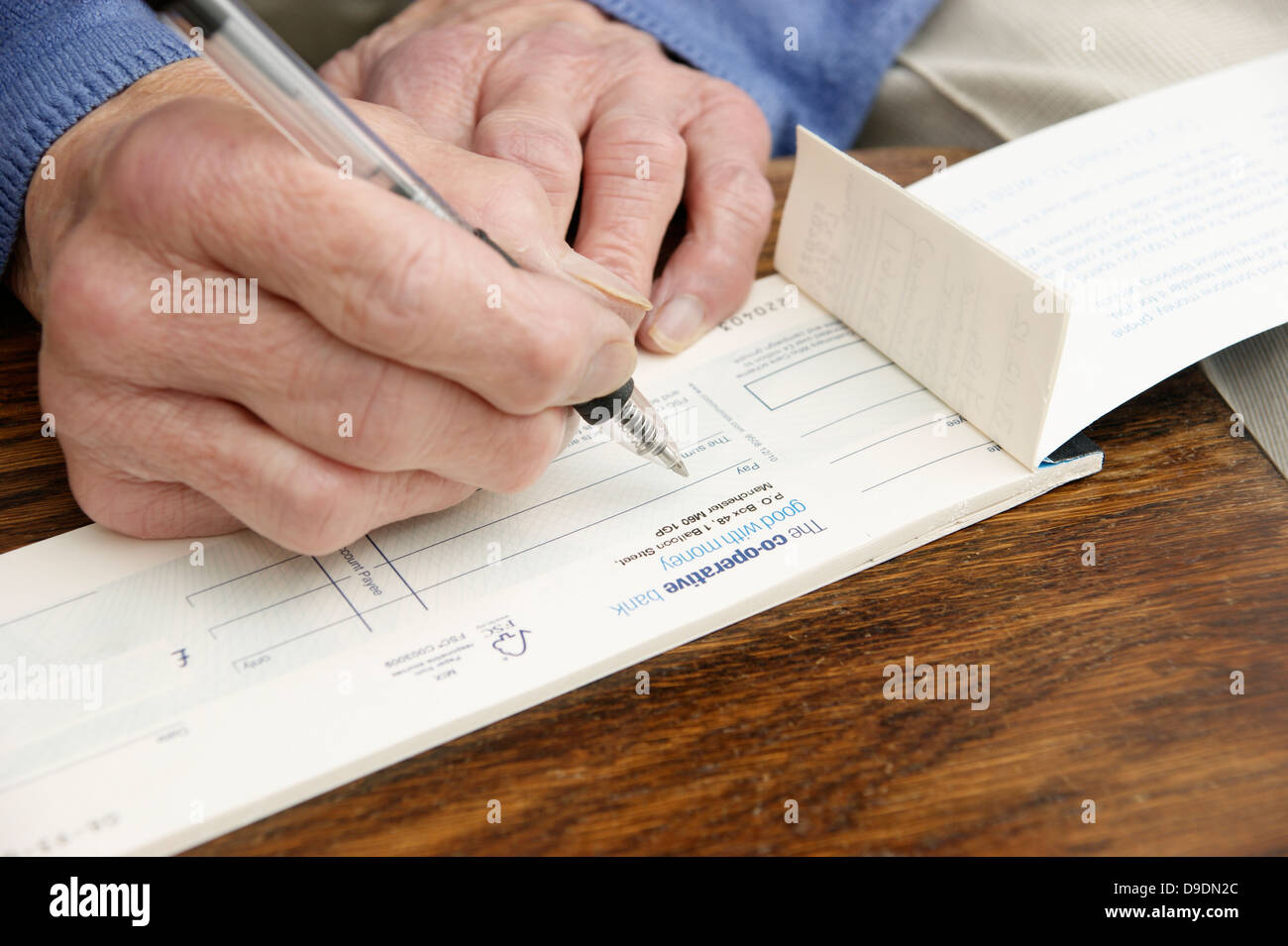 Donna anziana la scrittura di un controllo che è sempre più raro in questi giorni (Co-operative bank check book) Co operativa facce banca nazionalizzazione) Foto Stock