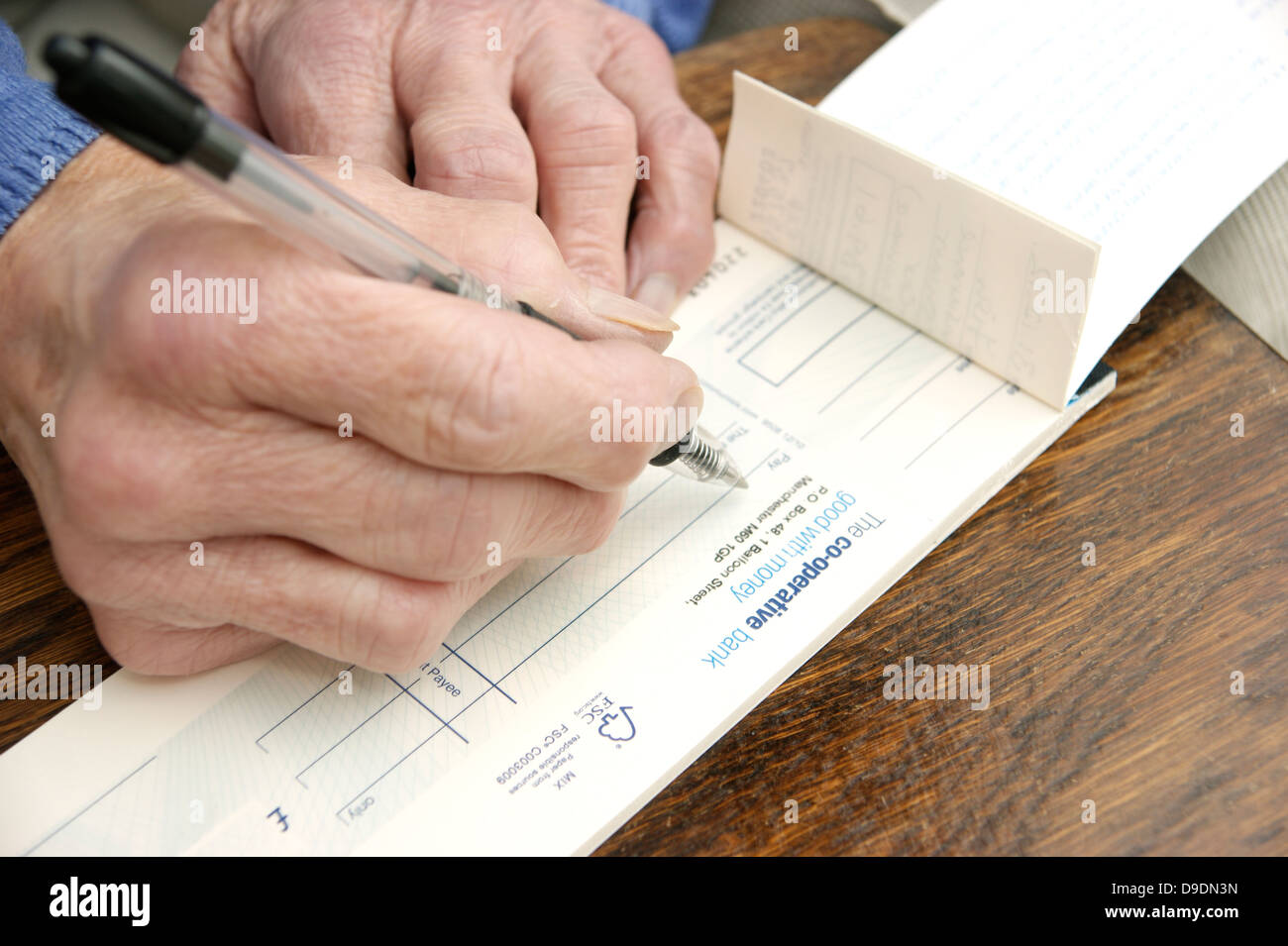 Donna anziana la scrittura di un controllo che è sempre più raro in questi giorni (Co-operative bank check book) Co operativa facce banca nazionalizzazione) Foto Stock