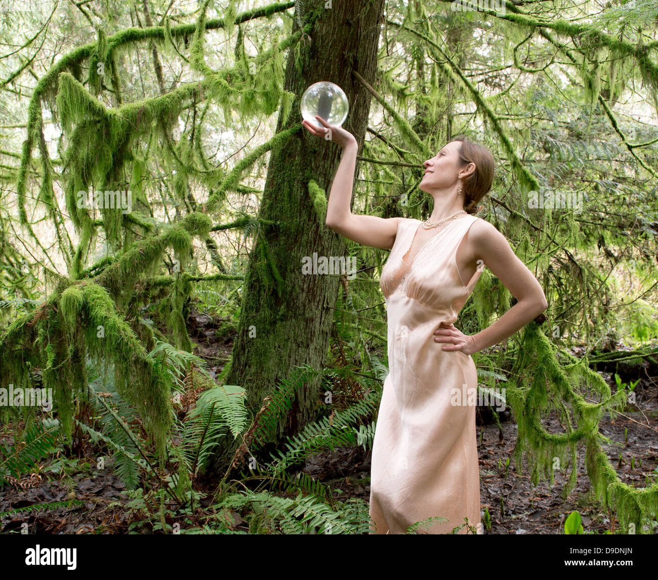 Donna matura guardando nella sfera di cristallo in foresta Foto Stock