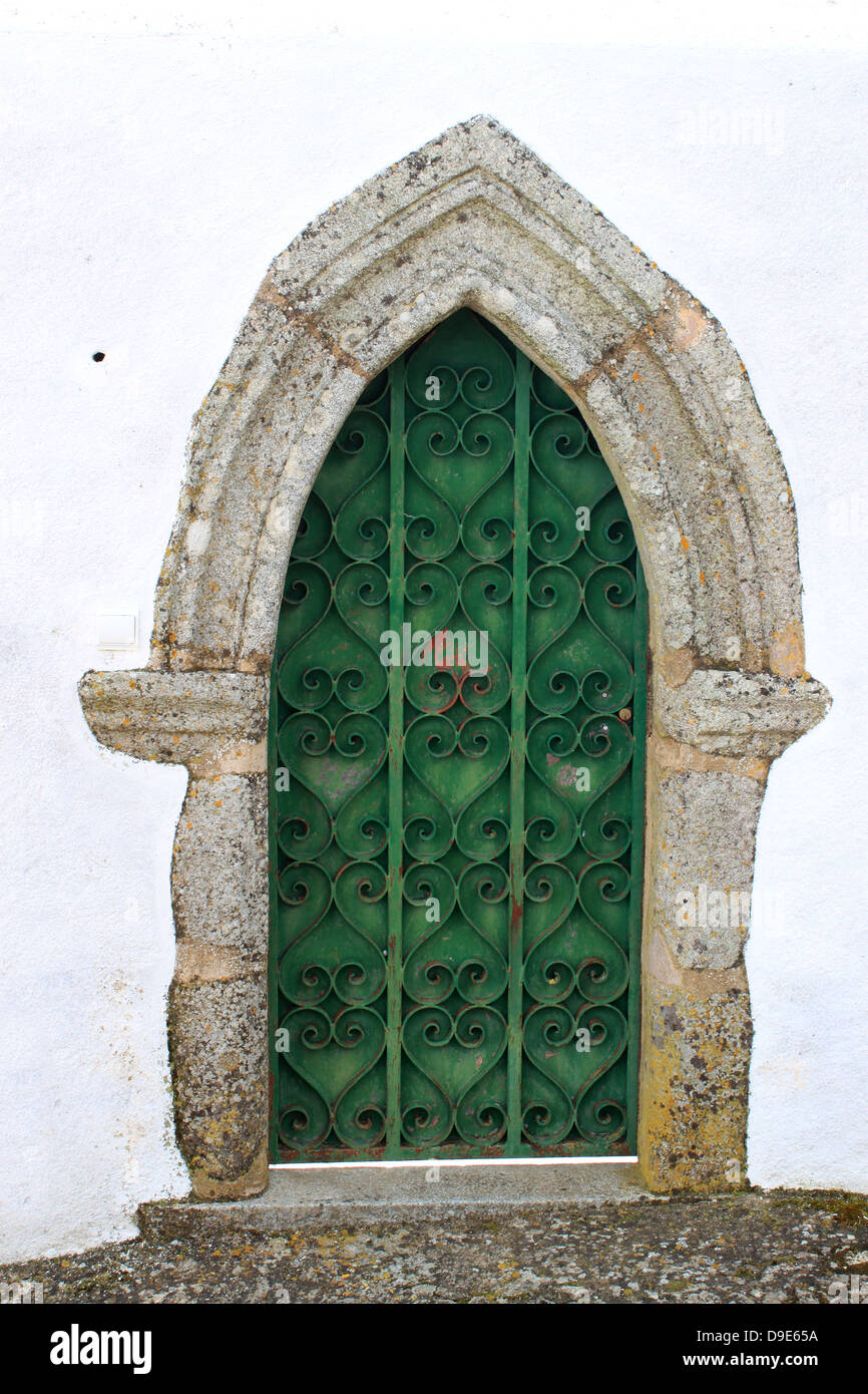 Green medievale porta in legno con ornati in ferro battuto che passa per un punto in alto su un bianco parete lavato Foto Stock