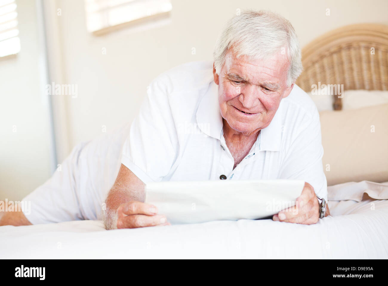Senior uomo disteso sul letto e quotidiano di lettura Foto Stock