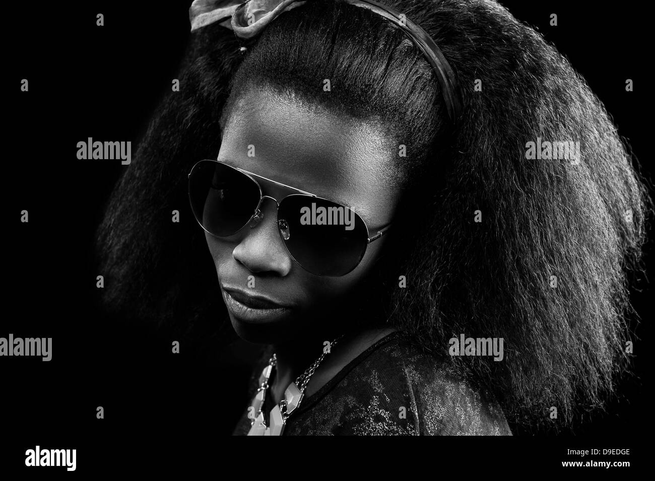 Giovane donna africana con occhiali da sole e afro capelli con una chiave di basso, sfondo bianco & nero studio shot. Foto Stock