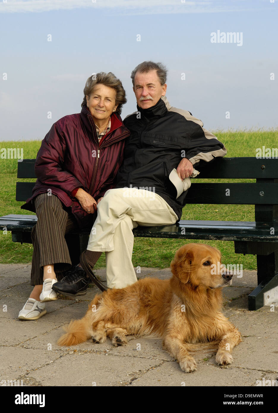 Senior Citizen's coppia siede su un parco-banco, prima di loro si trova il suo cane (modello di rilascio) Foto Stock