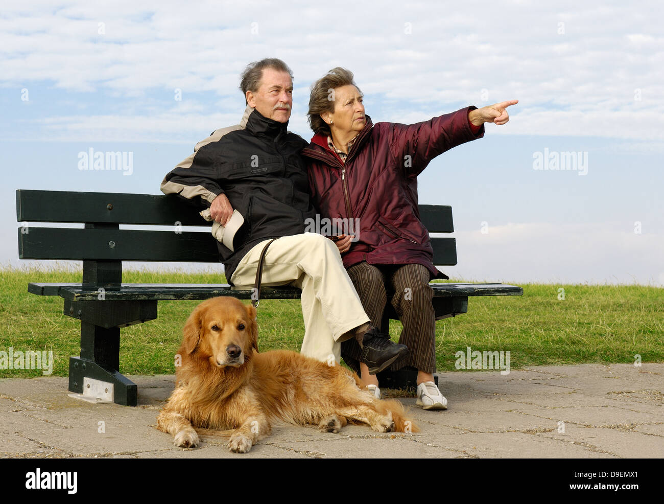 Senior Citizen's coppia siede su un parco-banco, prima di loro si trova il suo cane (modello di rilascio) Foto Stock