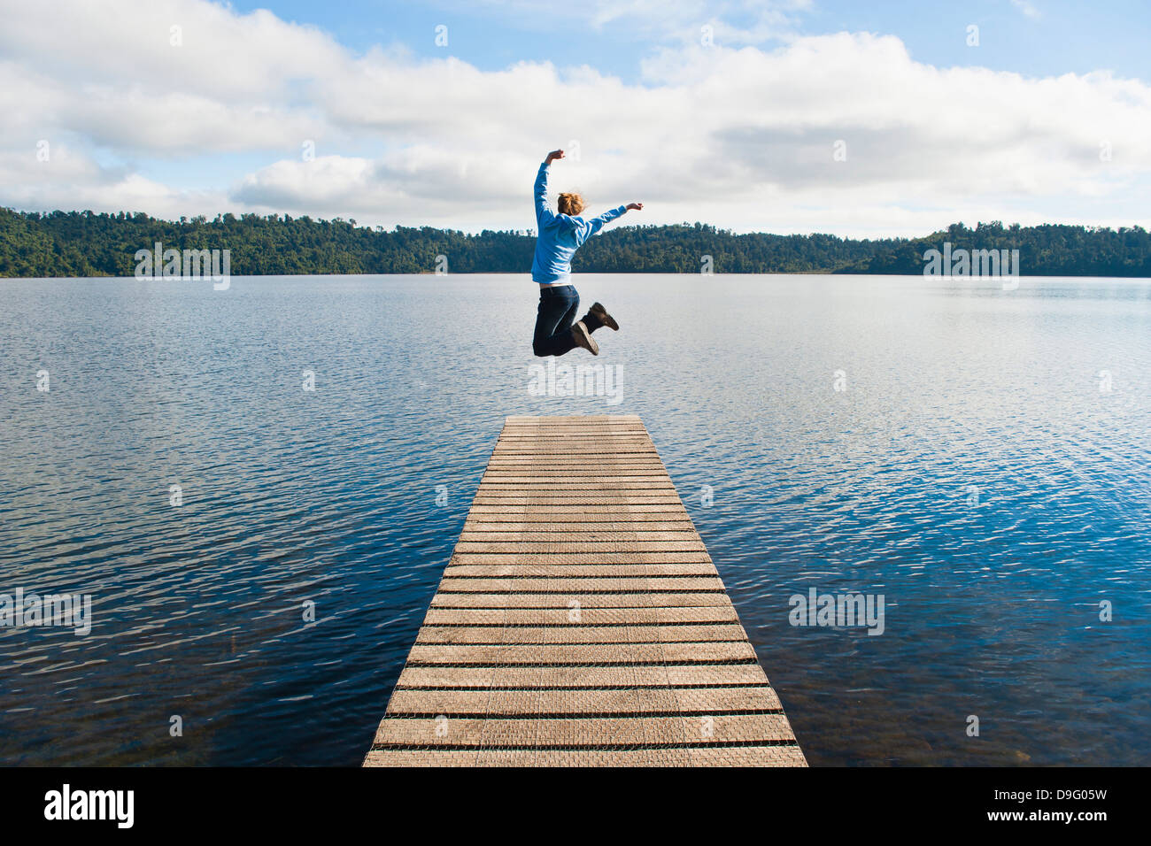 Donna salta su un molo al Lago di Ianthe, nella costa occidentale dell'Isola del Sud, Nuova Zelanda Foto Stock