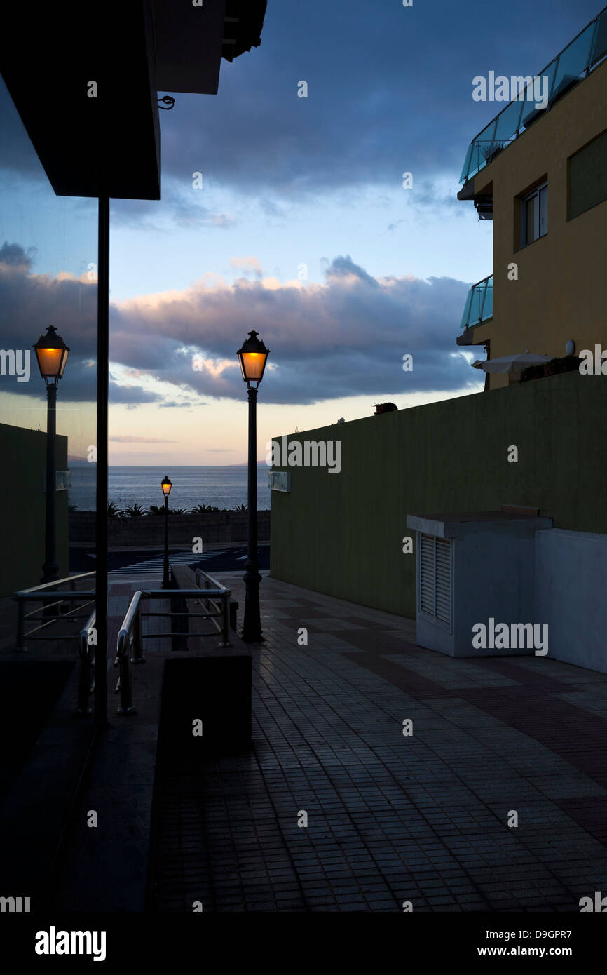 La mattina presto vista giù un vicoletto con luci di strada e di riflessione nella finestra di vetro, guardando verso il mare di Playa San Juan Foto Stock
