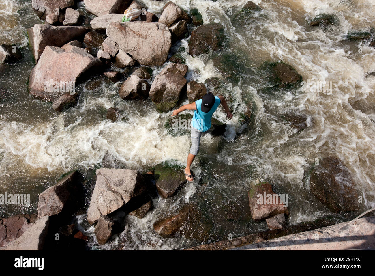 Un uomo tenta di attraversare le rocce per impedire Dulce fiume attuale vicino alla diga in Termas de Rio Hondo Foto Stock