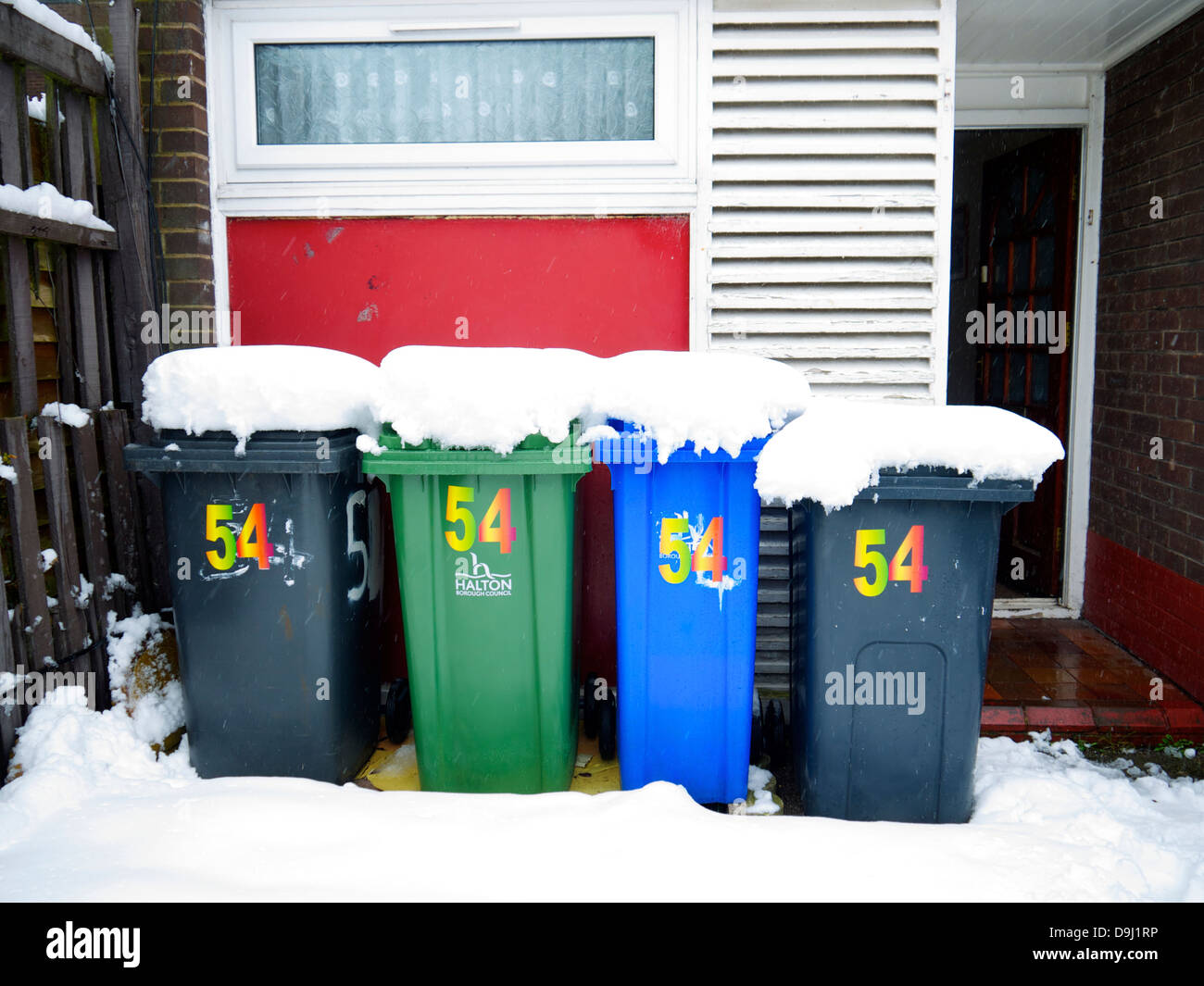 Scomparti wheelie fuori dalla casa, coperto di neve. Nero, Verde e contenitori blu. Foto Stock