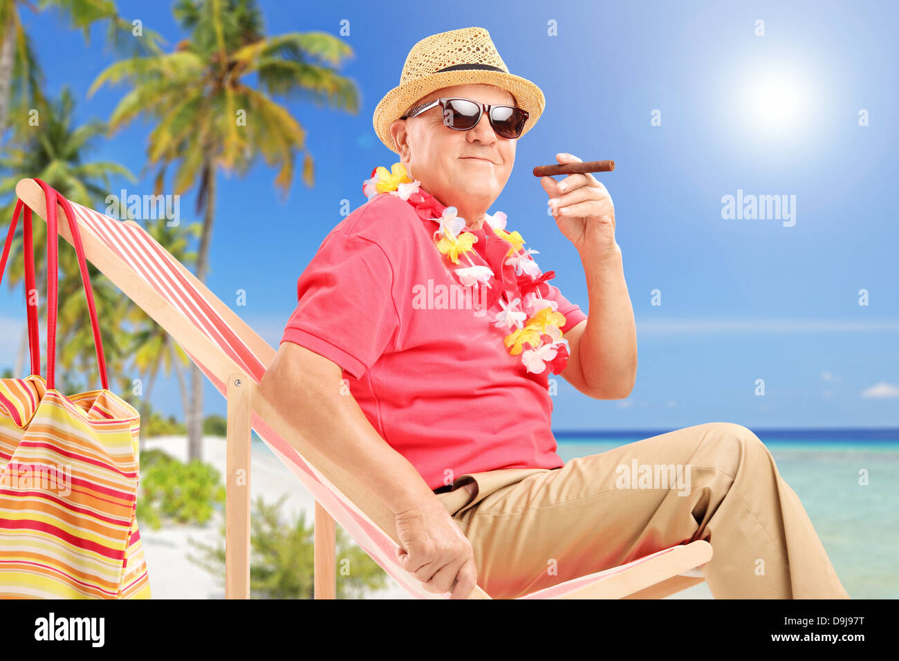 Gentleman di fumare un sigaro e godendo su una sedia a sdraio su una spiaggia tropicale accanto ad un mare e palme Foto Stock