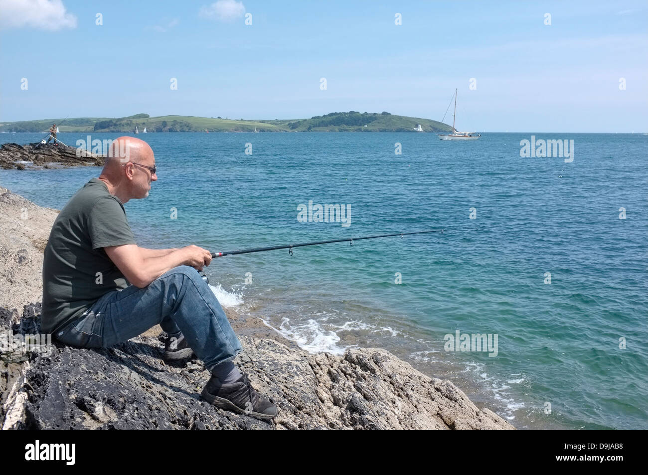 Un uomo pesca dal Pendennis Point in Falmouth, Cornwall Foto Stock