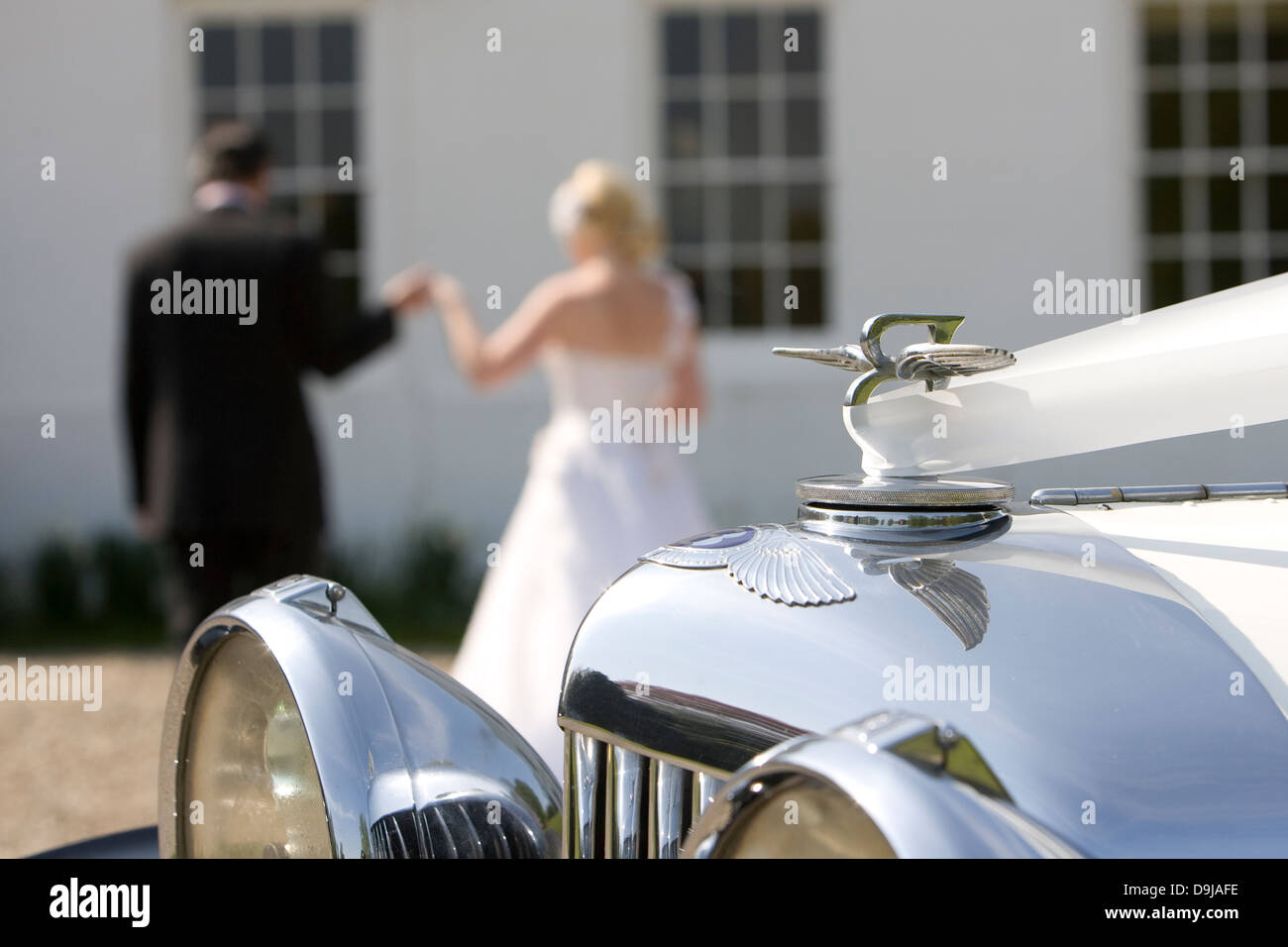 Dettaglio del matrimonio classico auto che mostra il simbolo e il proiettore con la sposa e lo sposo in background mantenendo le mani Foto Stock