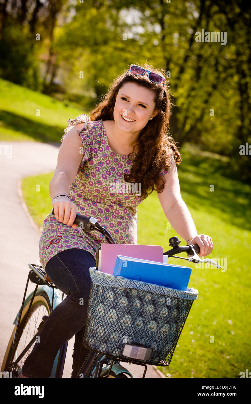 Giovane studentessa caucasica che guida una bicicletta tradizionale in stile shopper attraverso un parco britannico in estate. Foto Stock