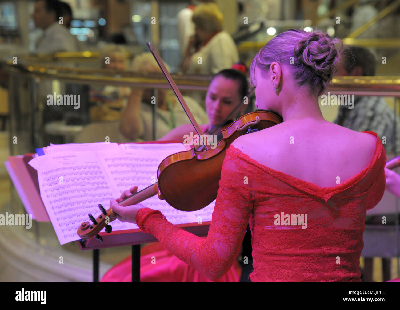 Signora violinisti giocare. Profondo rosso abiti e moody magenta evidenziazione su argomenti. Foto Stock