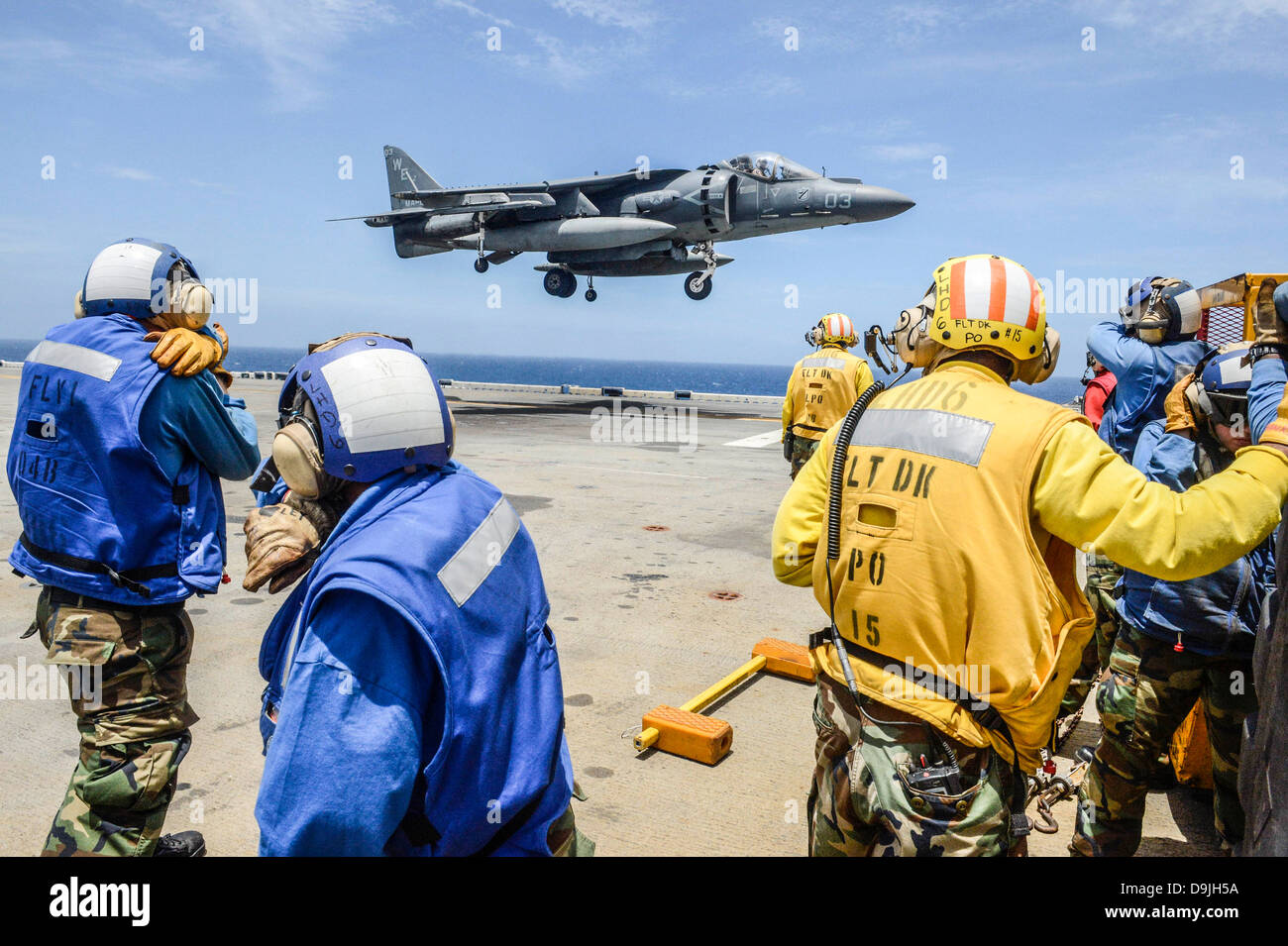 US Navy marinai a Amphibious Assault nave USS Bonhomme Richard scudo le loro facce da jet scarico come un AV-8B Harrier jet atterra sulla nave del ponte di volo Giugno 19, 2013 operanti nel Mar Cinese Orientale. Foto Stock