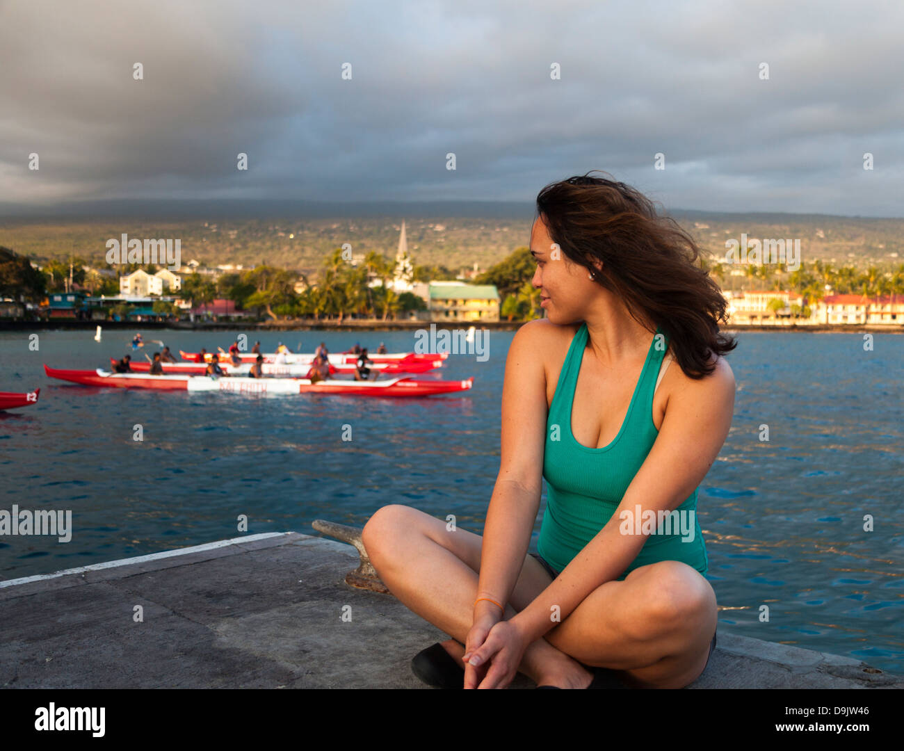 Donna seduta sul molo di Kailua-Kona sulla Big Island delle Hawaii guardando canoe outrigger Foto Stock